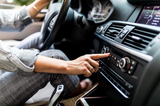 Woman adjusting the vehicle's air conditioning system while driving.